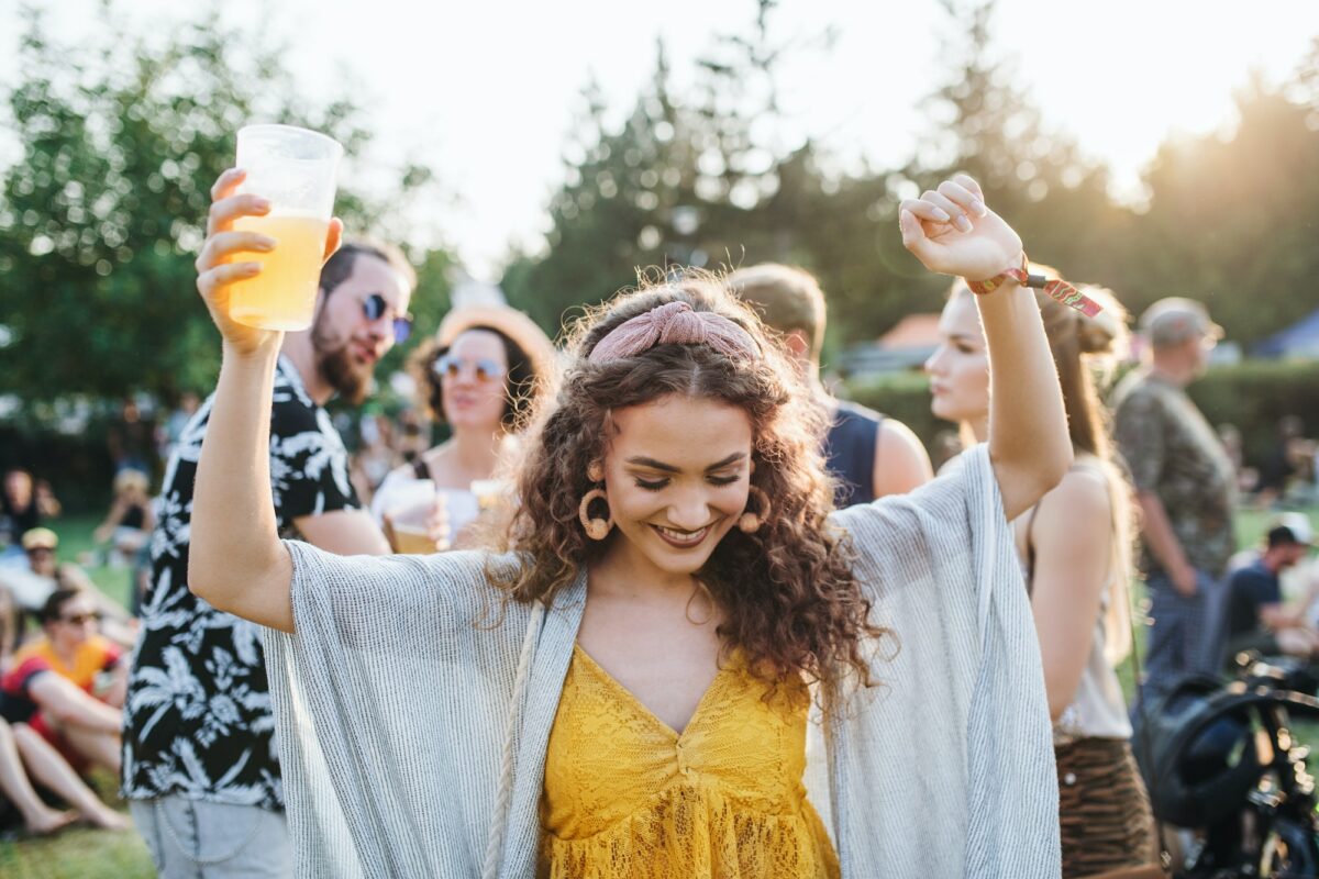 A young woman with drink dancing at summer festival